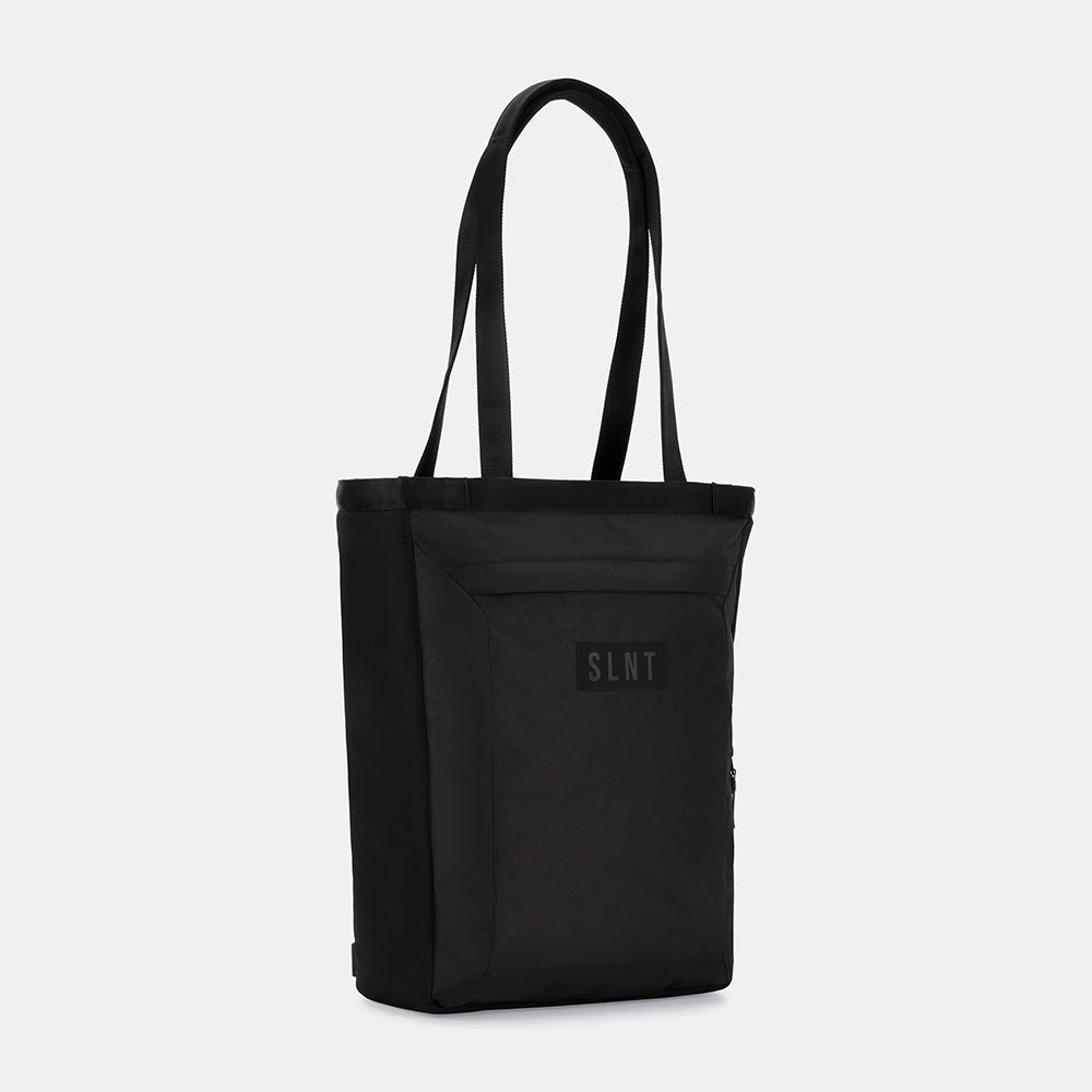 The SLNT E3 Faraday Tote Bag (17L) is a black, minimalist tote with two long handles, a front pocket, and a SLNT-branded patch. Photographed against a white background.