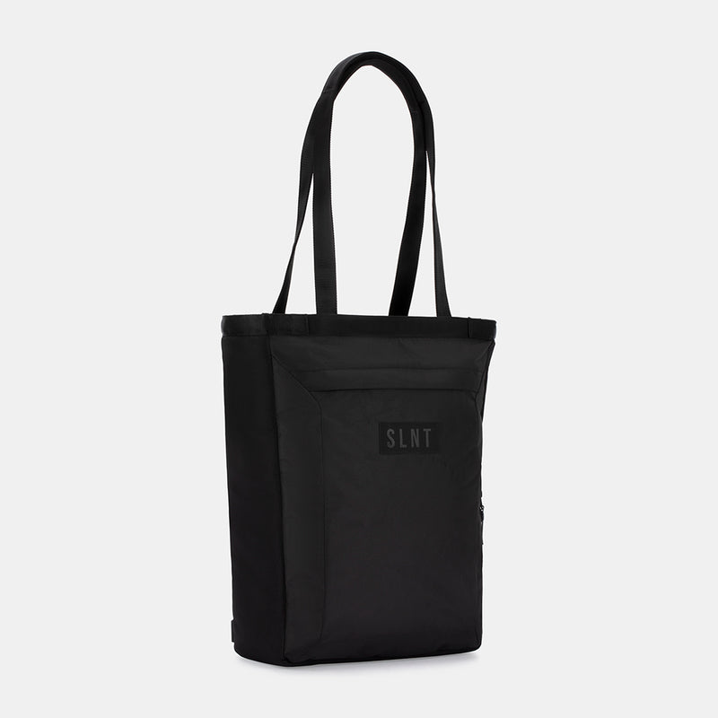 The SLNT E3 Faraday Tote Bag (17L) is a black, minimalist tote with two long handles, a front pocket, and a SLNT-branded patch. Photographed against a white background.